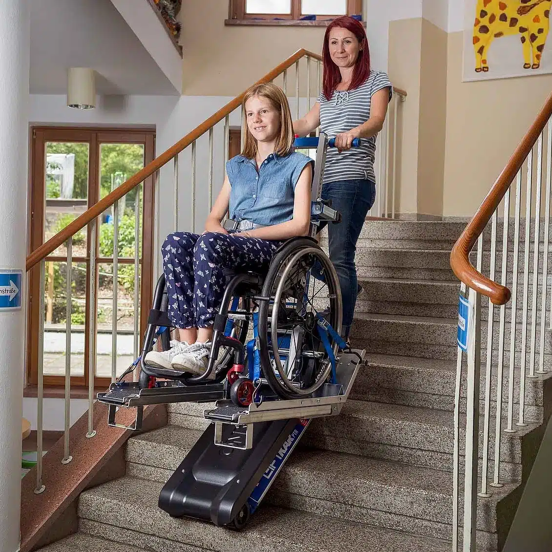 Frau hilft Mädchen im Rollstuhl mit Treppenraupe die Treppe hinauf