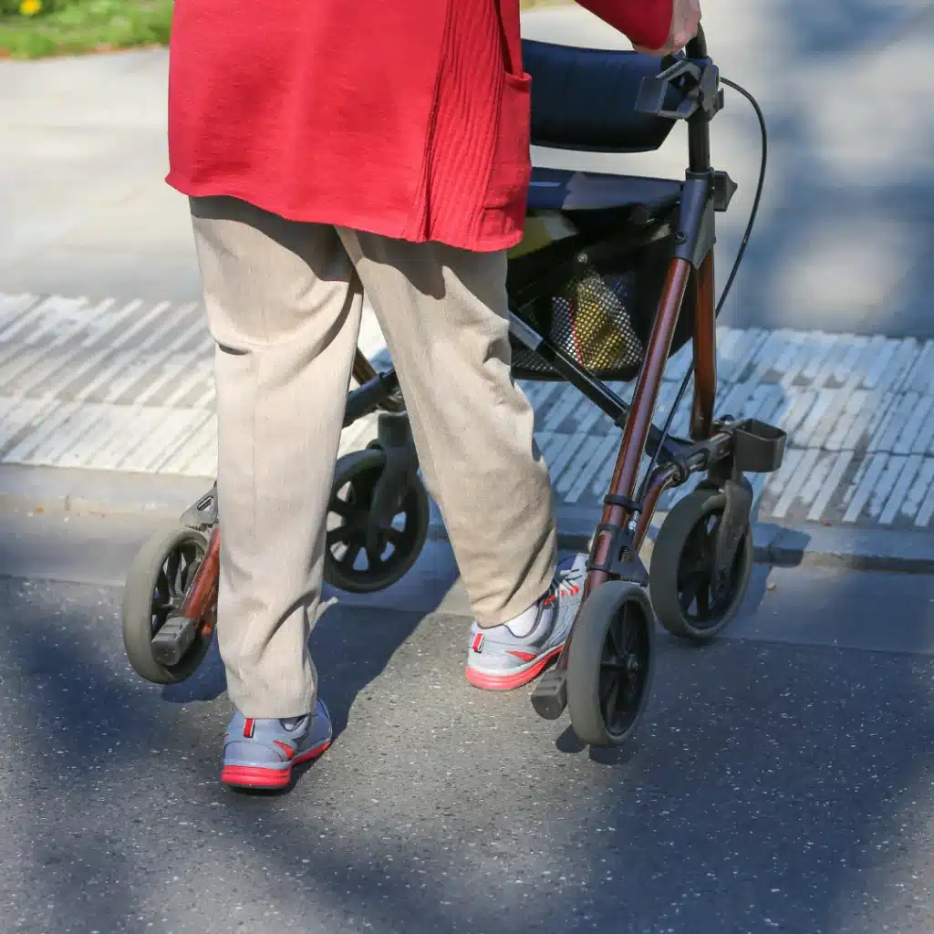 Frau läuft mit Rollator für außen die Straße entlang