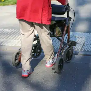 Frau läuft mit Rollator für außen die Straße entlang