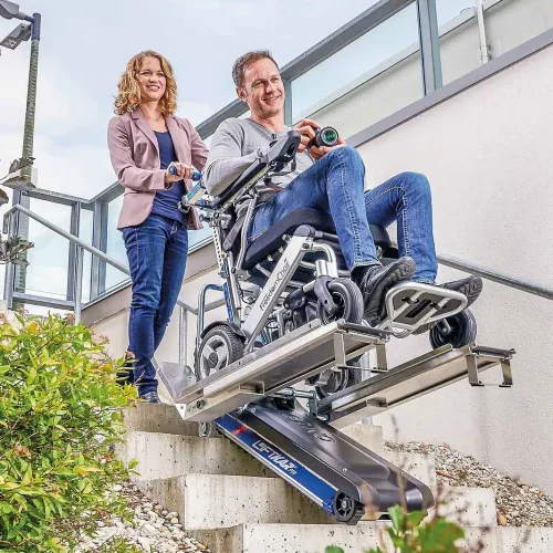 Frau hilft Mann im Rollstuhl mit Liftkar Treppenraupe die Treppe hinab