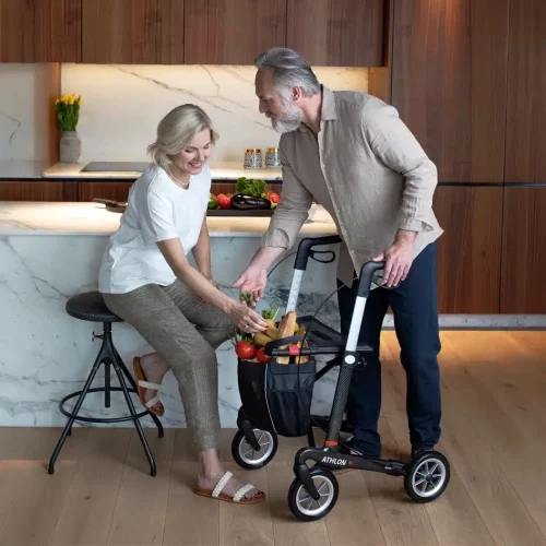 Senior mit Rollator, Frau greift nach Einkäufen in der Tasche des Rollators