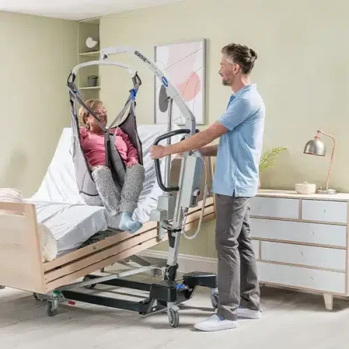 Pfleger hilft Seniorin mit Bettlifter ins Pflegebett